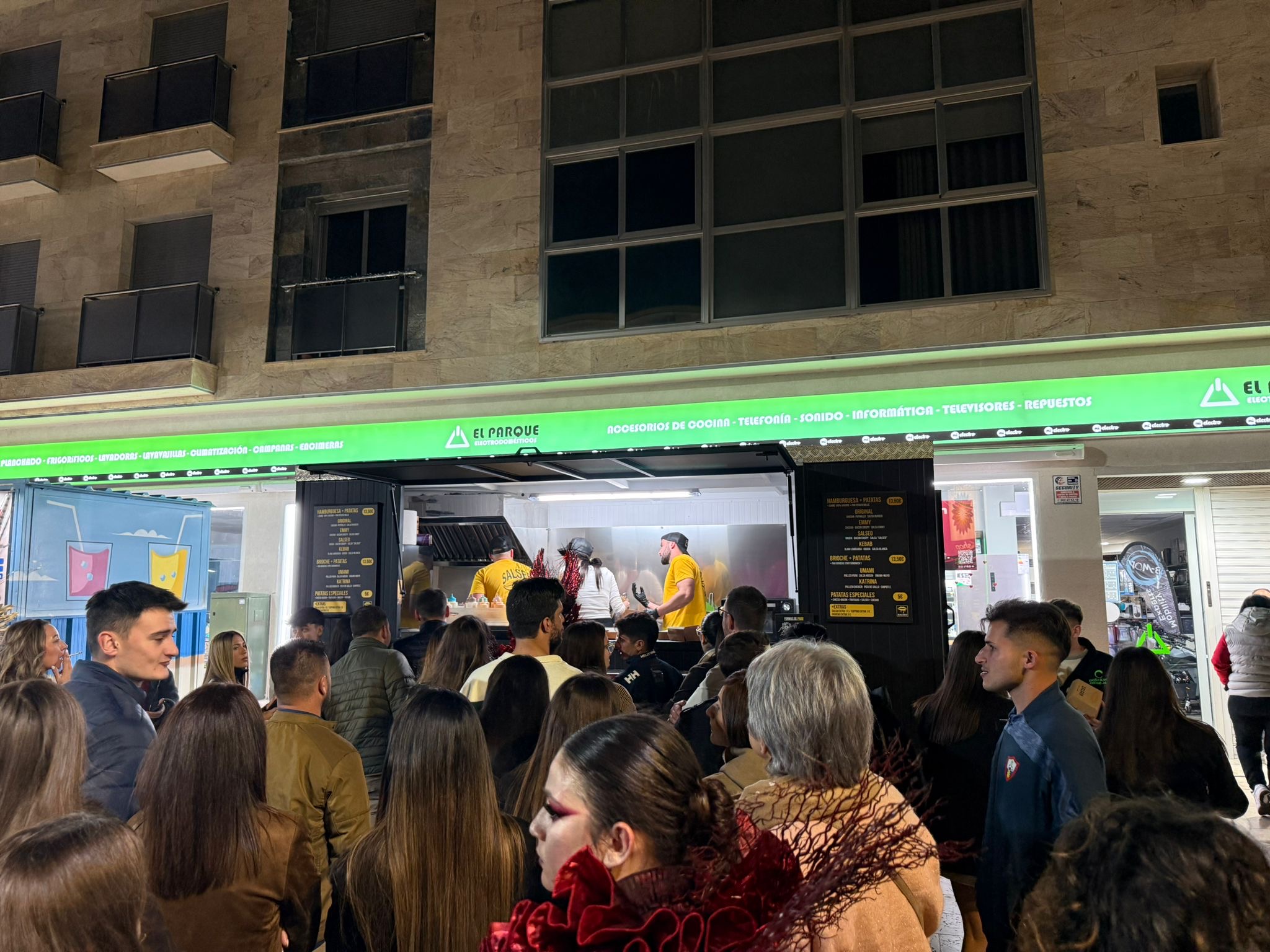 Puesto de comida iluminado en un evento, con clientes delante